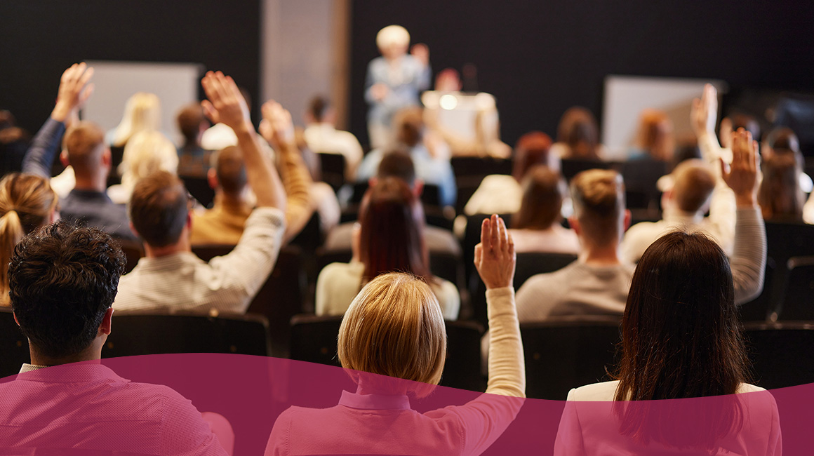 DLAC Presentations 2025 A group of people at a conference all raising their hands while staring at a stage where someone is talking