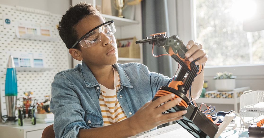 Student assembling a robotic arm at a desk with tools and parts in a bright, modern learning space.