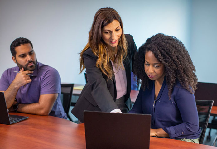 Woman helping another woman use a computer while a man at another computer watches