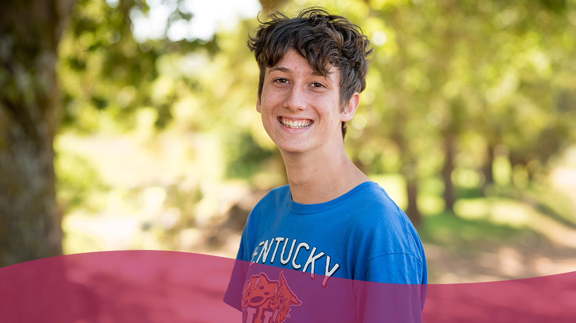 Thrive School student, Waldo, surrounded by trees in a blue shirt and smile on his face