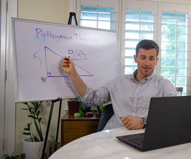 Teacher pointing to a white board with an illustration as they talk to someone via their computer
